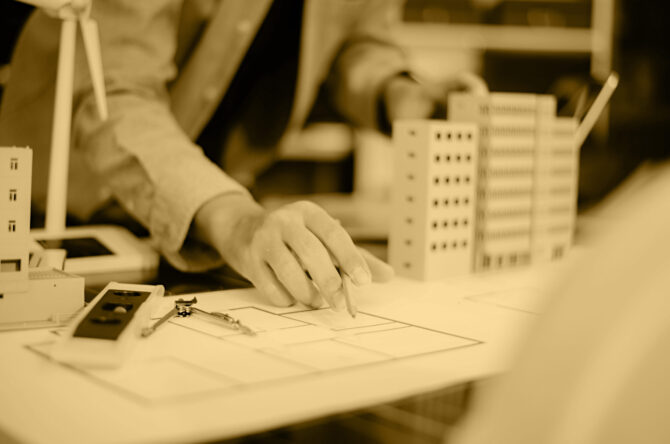 Engineer using compass on building plan with laptop, model, and wind turbine. Ideal for clean energy, architecture, sustainability, and smart city design themes